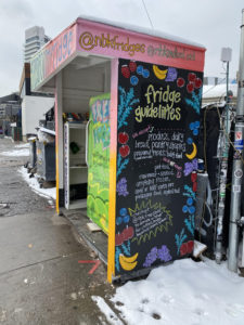 An outdoor multicolor booth housing a green refrigerator and white shelf