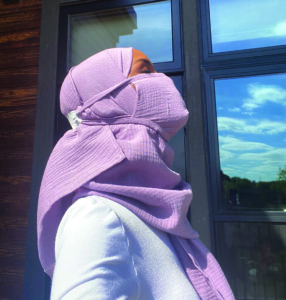Profile of woman wearing a light mauve hijab with matching colored face mask