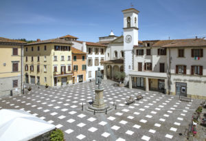 A plaza with numerous white squares painted on the ground one-point-eight meters apart in a lattice design for social distancing. The square is surrounded by buildings and has a statue in the center