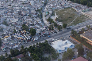 Aerial photograph of an urban environment showing small dense buildings on one side of a wide street and a blue and white angled hospital building on the other