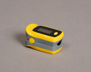 Yellow and gray rounded rectangular device with opening to insert a finger and an LCD screen on the top