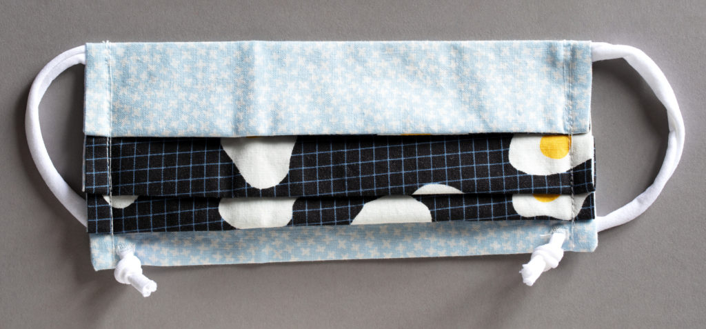 Rectangular pleated cotton face mask made up of light blue fabric patterned with stars and a gridded black fabric with stylized fried eggs