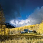 A photograph of a house in Telluride, Colorado. The house is surrounded by yellow-green trees dramatically lit by the sunlight.