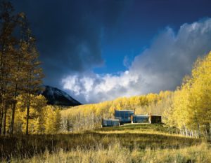 A photograph of a house in Telluride, Colorado. The house is surrounded by yellow-green trees dramatically lit by the sunlight.