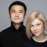 A photograph of a man and woman on a gray background both wearing black.