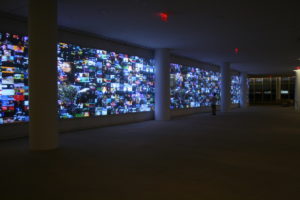 Perceptive Pixel's interactive screens are displayed along a wall. One person stands in the background looking at the screens.