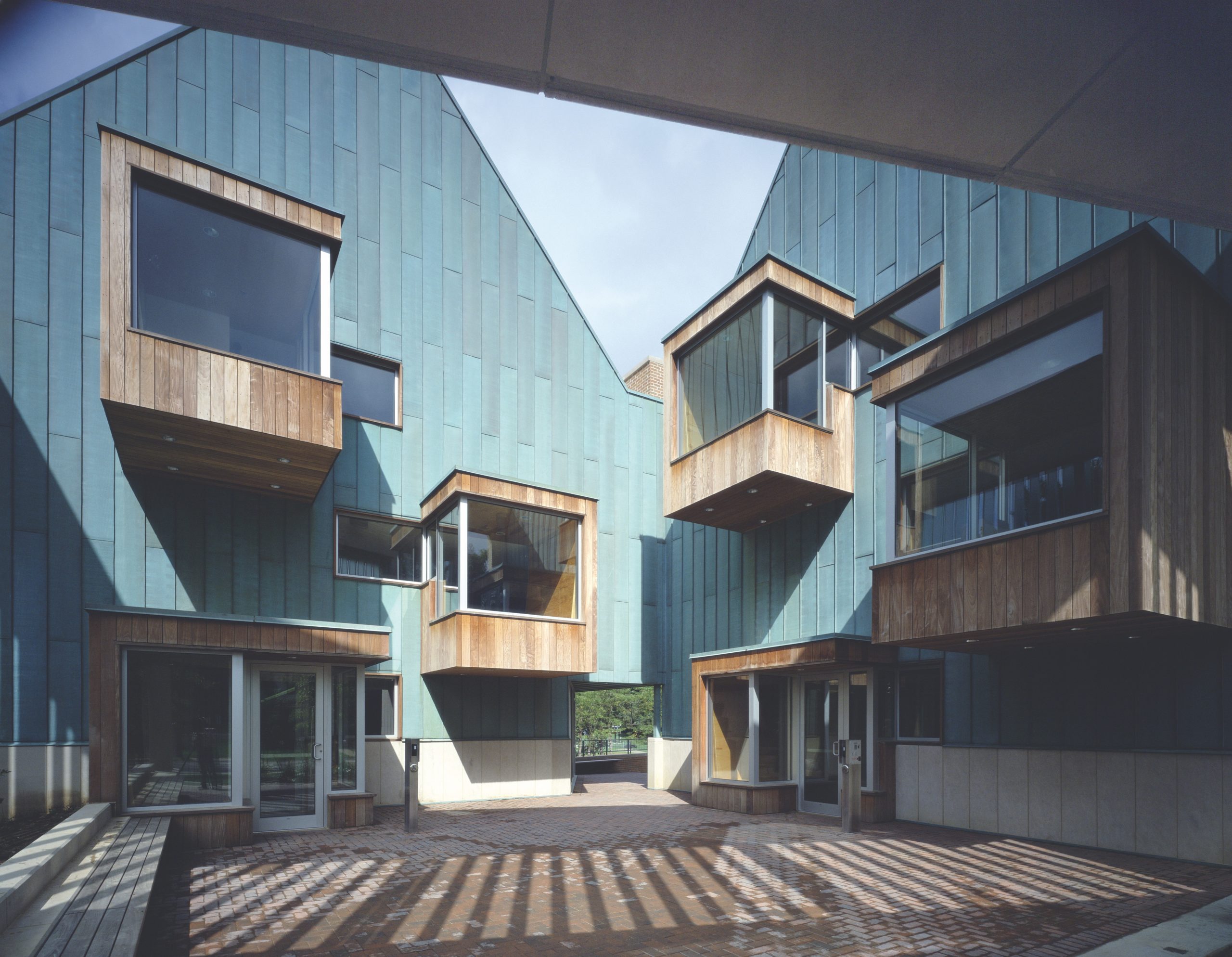 A photograph of a blue building with four square wooden structures protruding. Each wooden structure has a large window on two sides. There are two doors into the building each framed by similar wooden structures.