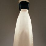 A strapless gown on a mannequin. The bust of the dress is black and the skirt is white. Where the two colors meet, a rectangle of cream fabric overlaps both at the center.