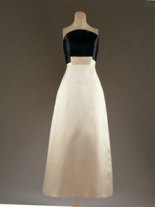 A strapless gown on a mannequin. The bust of the dress is black and the skirt is white. Where the two colors meet, a rectangle of cream fabric overlaps both at the center.