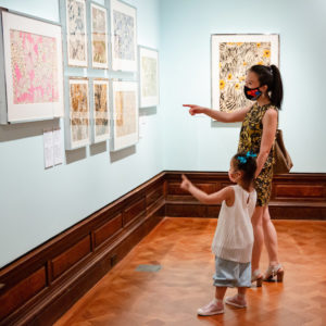 Two visitors, young and old, point at floral drawings in the museum galleries.