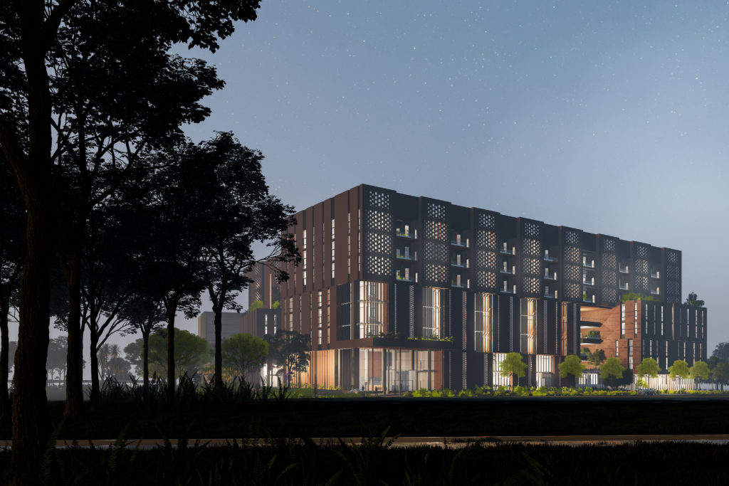 Distant exterior nighttime view of a long rectangular building that is brightly illuminated by windows of varying sizes across the full length of the building.