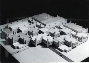 Black-and-white photograph looking down on an architectural model made up of overlapping rectangular and L shapes throughout a grid marked by vertical rectangular posts