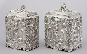 Rectangular silver box with scrolling organic designs surrounding scenic panels