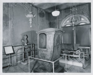Photograph of interior with a sculpture bust, furniture, and other objects on display in a gallery.