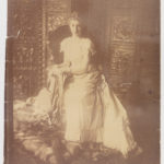 Photograph of a young lady sitting in a chair surrounded by other pieces of furniture.