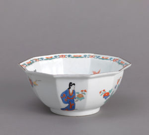An octagonal white porcelain bowl decorated with flowers and a human figure.