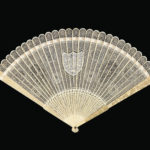 Delicate lace-like carved ivory fan, spread open on a black background