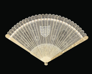 Delicate lace-like carved ivory fan, spread open on a black background