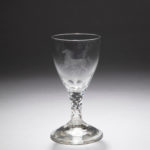 Clear-glass wine glass with a wide rim, tapering body, thick stem accented with triangular crystallized segments, and a broad round base, a translucent galloping horse set against thin leafy trees is etched into the surface of the bowl