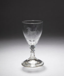 Clear-glass wine glass with a wide rim, tapering body, thick stem accented with triangular crystallized segments, and a broad round base, a translucent galloping horse set against thin leafy trees is etched into the surface of the bowl
