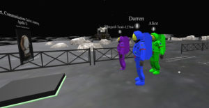 Three players' avatars in space suits that are bright shades of purple, blue, and green, stand in the moonscape in front of a floating image of a "communications device" from Apollo 11. Each player's name floats above their avatar's head. A black fence, scattered moon boulders and a moon lander are visible in the background.