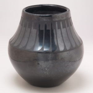 Black glazed ceramic vessel with tall sides curved inwards and subtle motif of abstract knife shapes in a row around the top.
