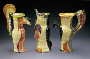 Three tall, glazed vessels with dramatic plum-like handles painted in beige, dark green, brown abstract shapes.