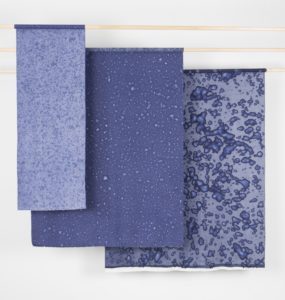 Three textiles pieces, each a different shade of blue, with waterdrops embedded into each textile.