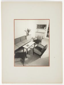 Black and white photo of a sleek living area featuring three armchairs and a flat, simple couch facing inward towards a small rectangular coffee table.