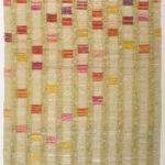 Vertical columns of light golden thread run down the length of a long textile, with vibrant squares of pink, purple, red, and yellow cascading down the columns.