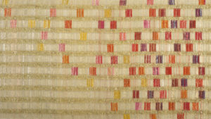 Vertical columns of light golden thread run down the length of a long textile, with vibrant squares of pink, purple, red, and yellow cascading down the columns.