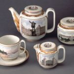 A four-piece porcelain tea set decorated with highly-detailed depictions of different landmarks in Leningrad and accented with ornate gold designs.