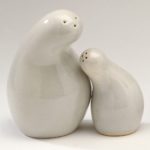 Two white ceramic salt shakers with rounded bodies that curve into each other, evoking a mother and child leaning into each other for an embrace.