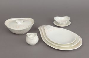 A set of white ceramic dishware with subtly curving edges reminiscent of flowers opening, decorated with clusters of thin black lines surrounded by explosions of tiny pink and orange dots like bunches of delicate flowers.