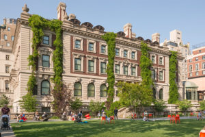 View of the Carnegie Mansion from the house's garden, with green foliage on its facade and orange chairs in the grass.