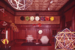 Photograph of a museum exhibition of geometric structures in a room with brown woodwork.