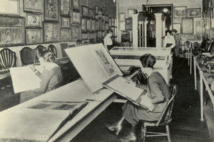 Black and white photograph of a group of students in a room studying different parts of a collection of art.
