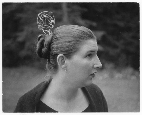 Black and white photo of a woman with her hair in a bun wearing a spherical sculpture in her hair.