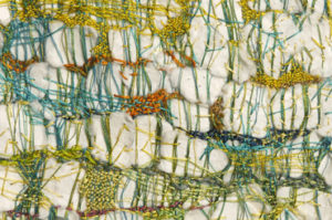 Thick, white, cloud-like fabric is wrapped in an uneven, net-like pattern of thin, colorful threads.