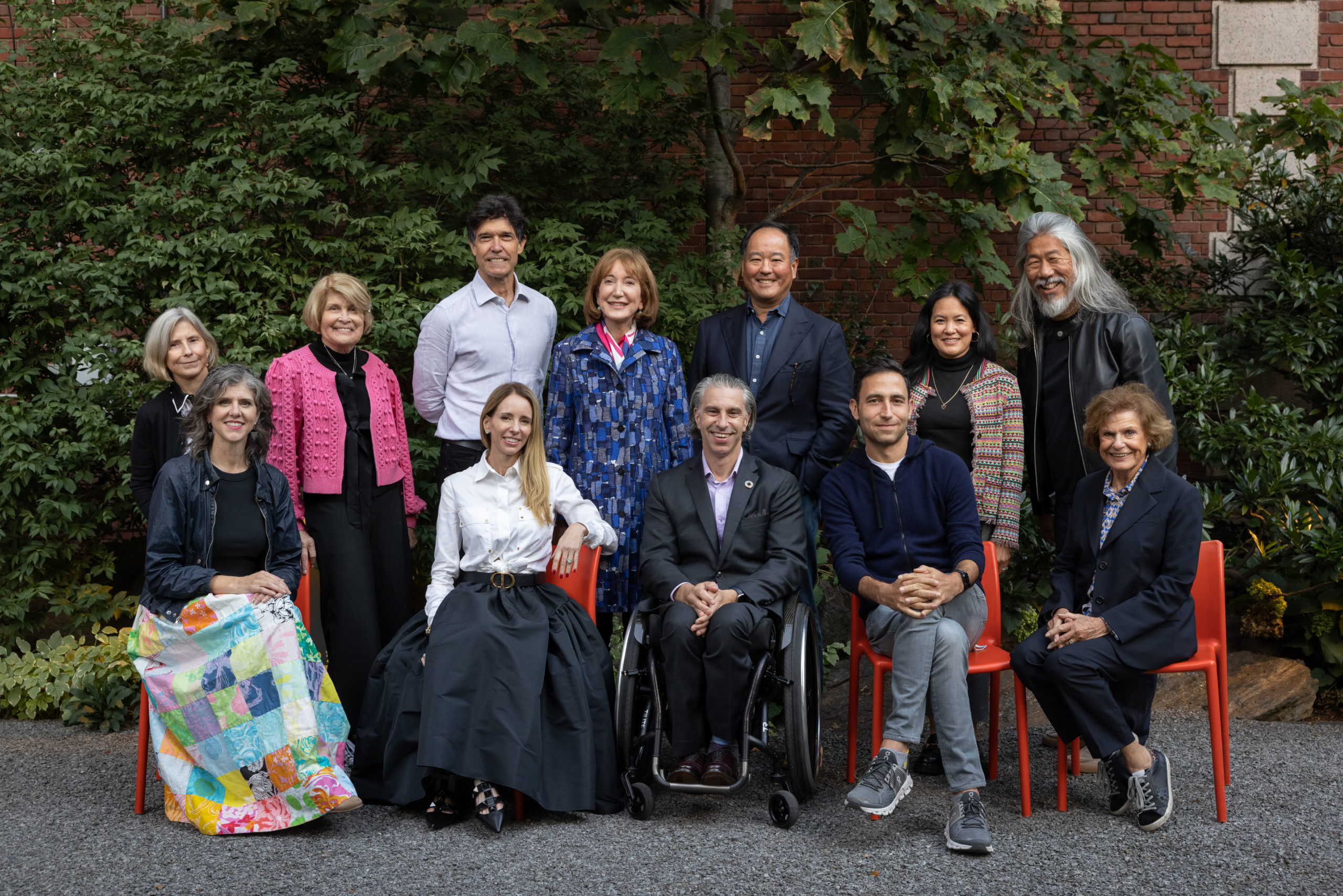 Twelve people, seven standing and five sitting, with green leaves in the background.