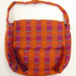Bright orange handbag with red tassels, decorated with columns of maroon squares and short, teal stripes of thread that form a checkerboard pattern.