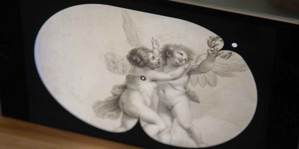 Close up shot of the finished Art Clock depicting an etching of two cherubs embracing that shows the time 2:30, with hour and minute hands aligned with angles in the etching.