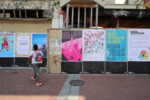 Large, door-sized posters are plastered along the outside wall of a relatively rundown building.