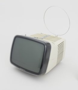 A small television set with a pronounced, gray-rimmed screen and beige body with a circular antennae extending above.