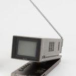 A portable television set that is rectangular. The screen portion pivots upward revealing buttons and controls, and a straight antennae extending upward at an angle.