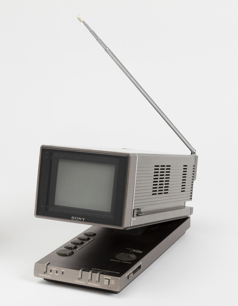 A portable television set that is rectangular. The screen portion pivots upward revealing buttons and controls, and a straight antennae extending upward at an angle.