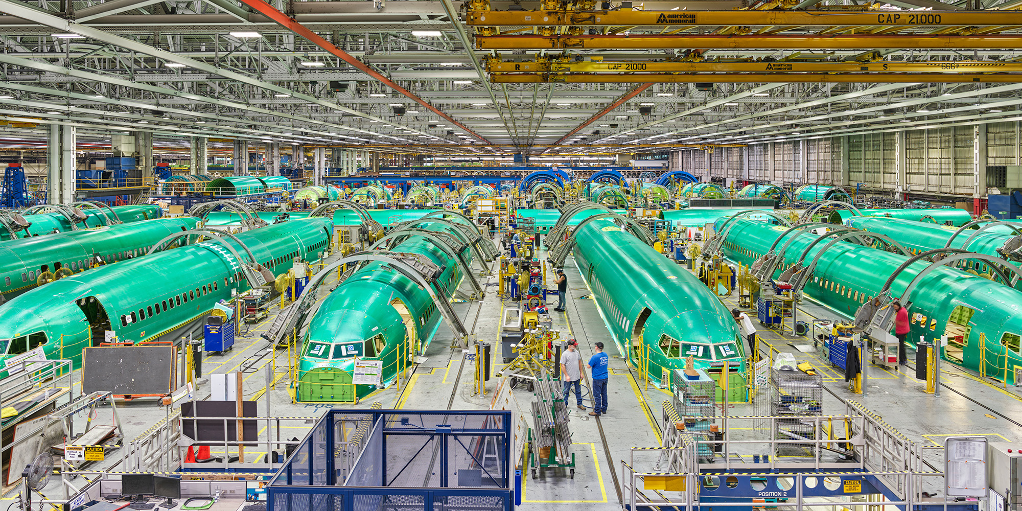 Wide shot of a factory floor featuring bright green Boeing 737 MAX fuselage sections.