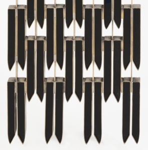 Close-up view of angular feathers made from black obsidian and connected by metal encasements.
