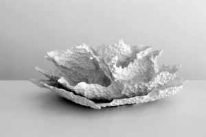 A white sculptural object, similar to the shape of a flower, with a thin structure and texture that looks sponge-like.