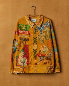 An orange button-up jacket with a Western feel covered in loud, colorful designs, including a neon motel sign with a cactus decoration, a teapot with two mugs, two people playing soccer, and a stamp that says [Pure Fresh Milk].